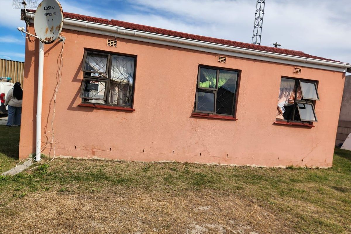Rear exterior view of a single-story house featuring a tiled roof, aluminium window frames with burglar bars, and a satellite dish installation.