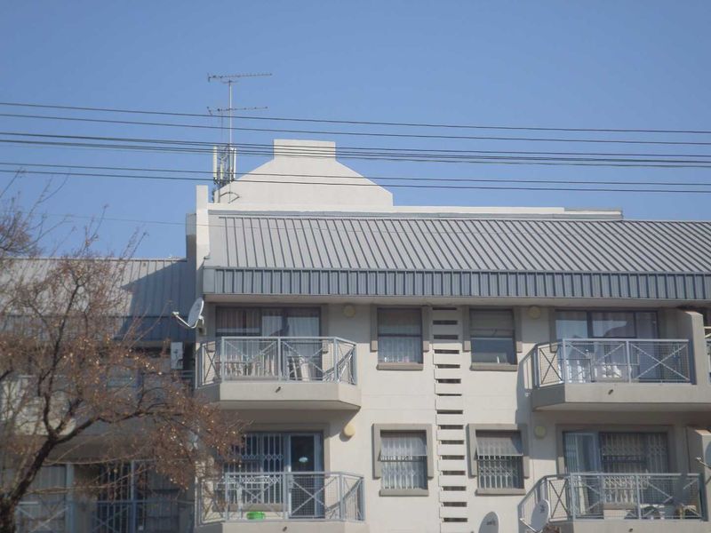 Exterior view of an apartment building facade featuring metal roofing, multiple balconies with security gates, and installed satellite dishes.