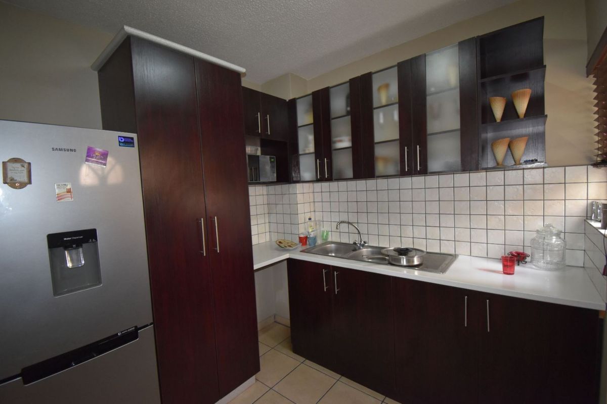 A functional kitchen featuring dark wood cabinetry, white countertops, a tiled backsplash, and a double-basin stainless steel sink.