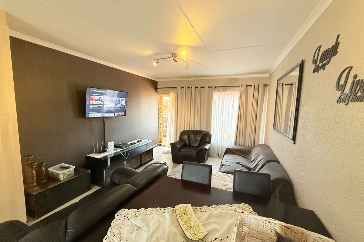 A living room featuring tiled flooring, ceiling coving, and track lighting, with direct access to an outdoor area through a glass door.