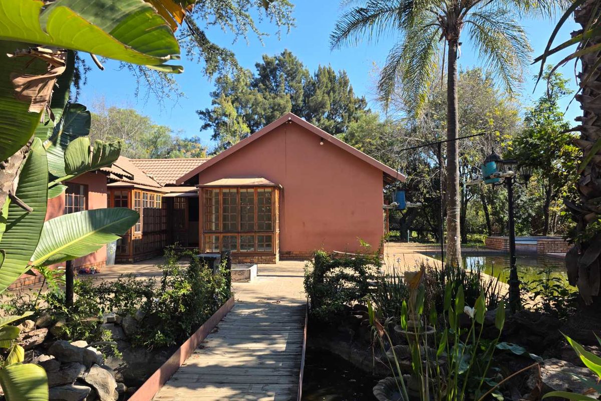 Rear view of the property featuring a tiled roof, wooden-framed sunroom, paved patio area, and a landscaped garden with a small pond and bridge.