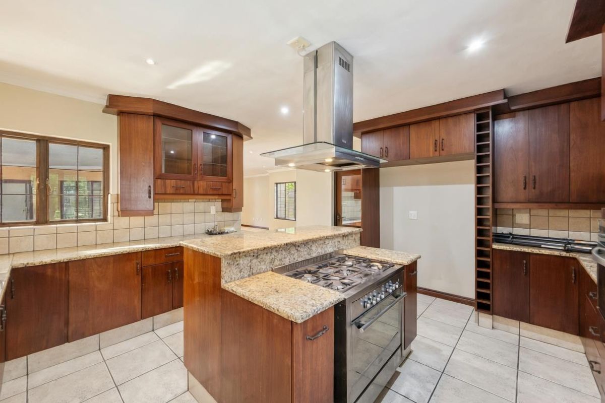 Spacious kitchen featuring dark wood cabinetry, granite countertops, a central island with a gas hob, and a stainless steel extractor fan.