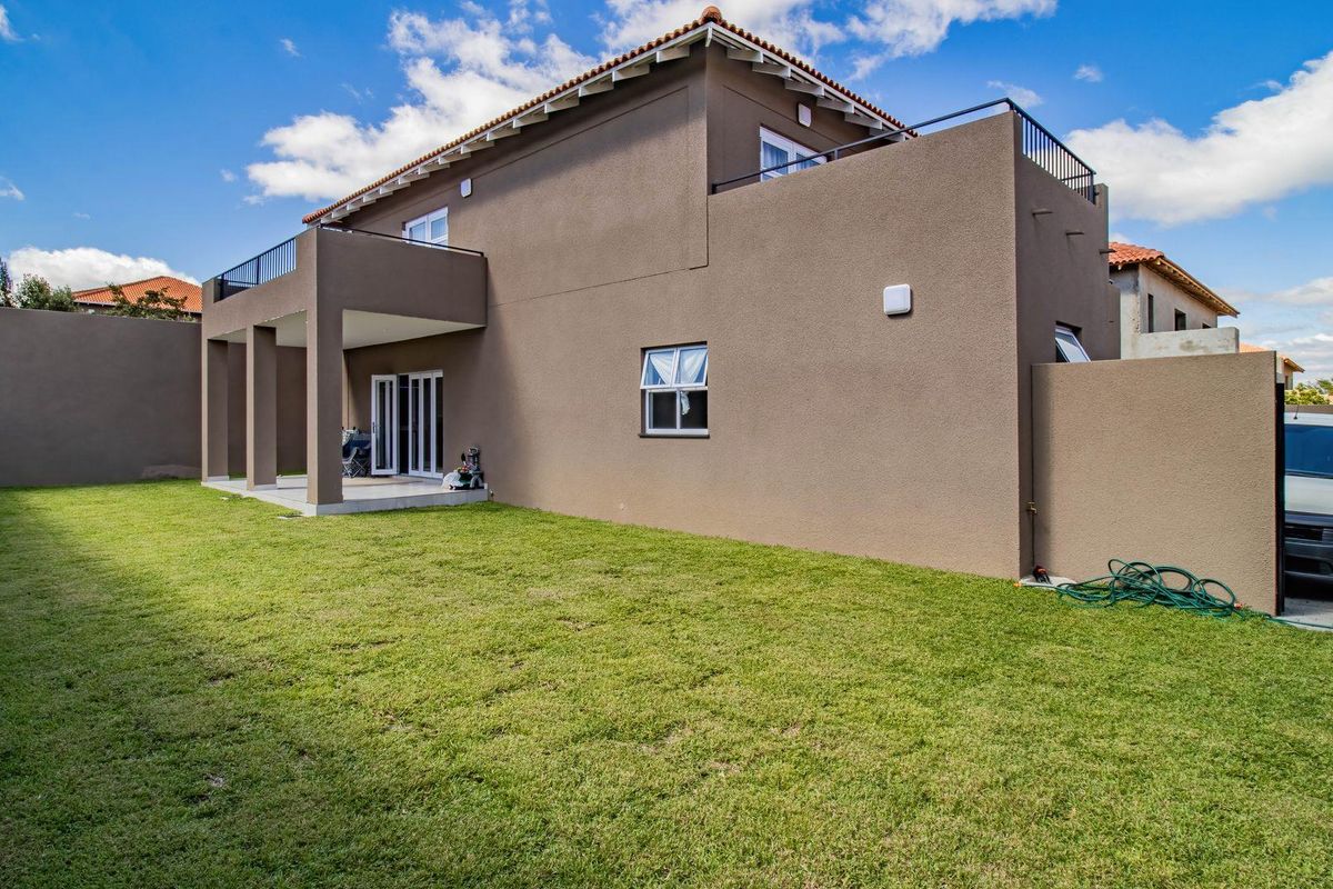 Rear view of the cluster home featuring a spacious lawn, covered patio, and an upper-level balcony with metal railings.