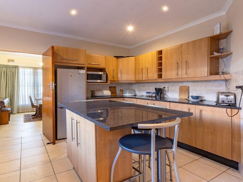 A functional kitchen featuring light wood cabinetry, granite countertops, a central island, and tiled flooring with recessed lighting.