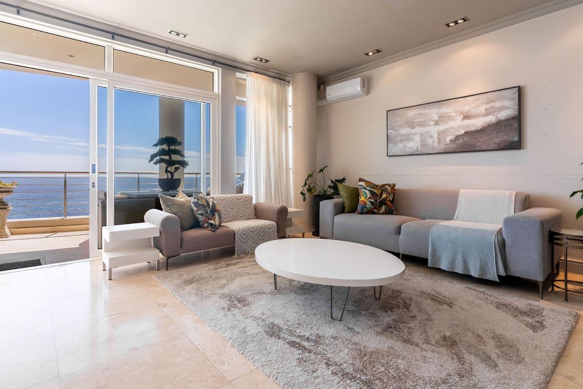 Bright living room featuring large sliding glass doors leading to a balcony with ocean views, tiled flooring, and a wall-mounted air conditioning unit.