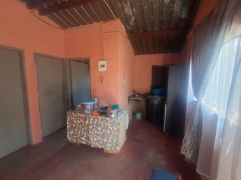 A basic kitchen area featuring exposed corrugated metal roofing, wall-mounted electrical distribution board, and a simple sink setup with unfinished wall surfaces.