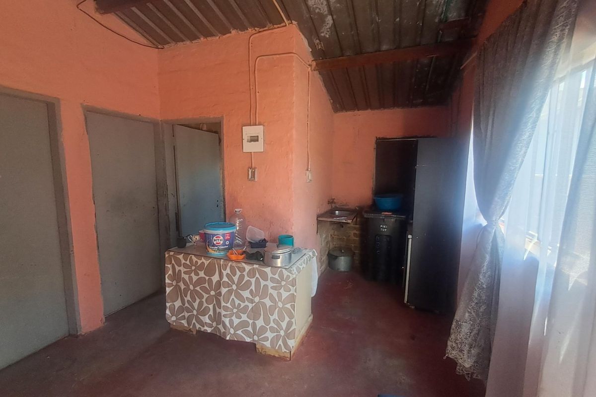 A basic kitchen area featuring exposed corrugated metal roofing, wall-mounted electrical distribution board, and a simple sink setup with unfinished wall surfaces.