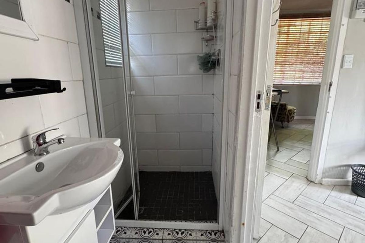 A functional bathroom featuring a shower enclosure, vanity basin, and patterned floor tiles, with a view into the adjacent room.