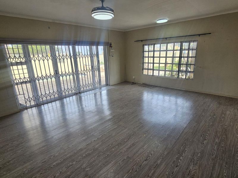 Spacious, empty living room featuring laminate flooring, large sliding glass doors with security gates, and grid-pattern windows providing natural light.