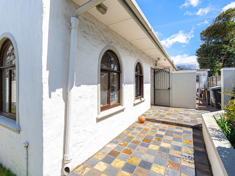 A rear exterior view featuring a tiled patio, arched windows with wooden frames, and a secure metal gate leading to the side yard.