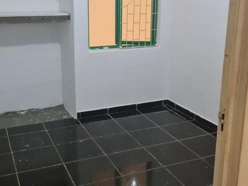 An empty bedroom featuring dark tiled flooring, built-in wall shelving, and a window fitted with security bars.