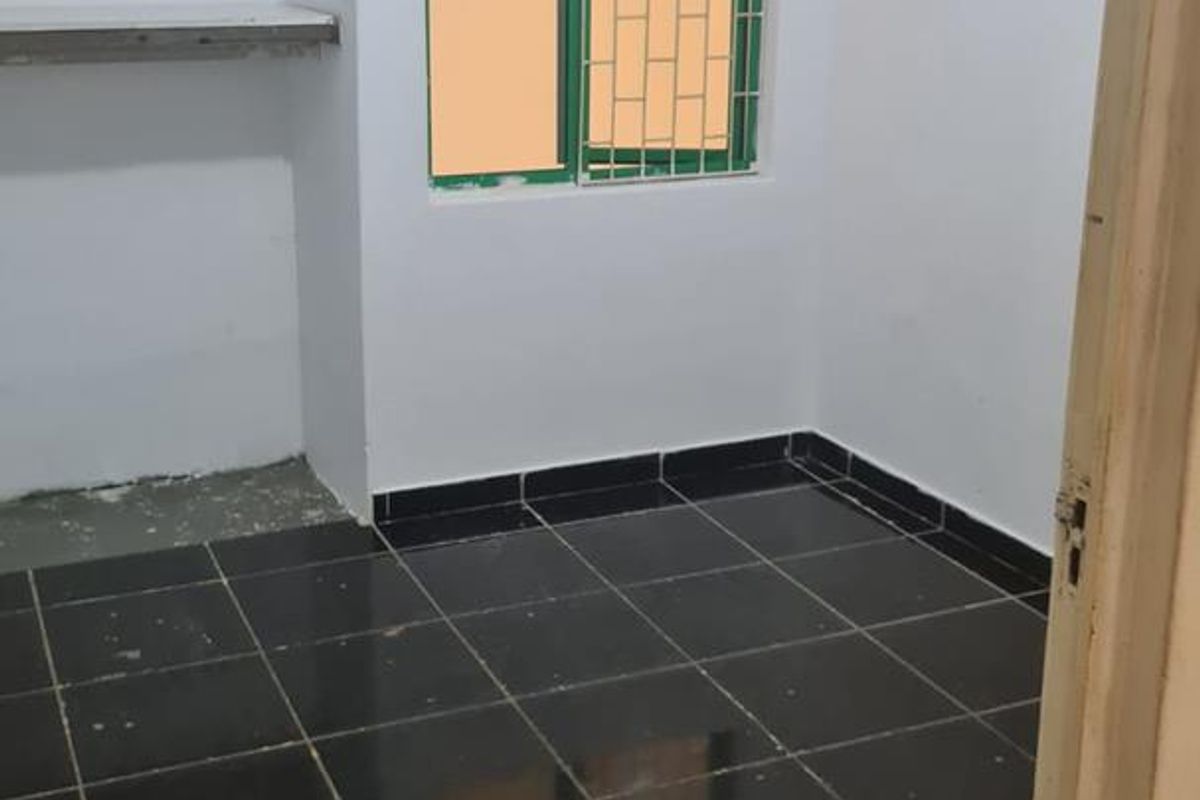 An empty bedroom featuring dark tiled flooring, built-in wall shelving, and a window fitted with security bars.