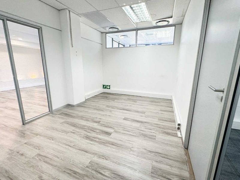 A vacant, well-lit office space featuring modern laminate flooring, a glass partition wall, and a suspended ceiling with recessed lighting.