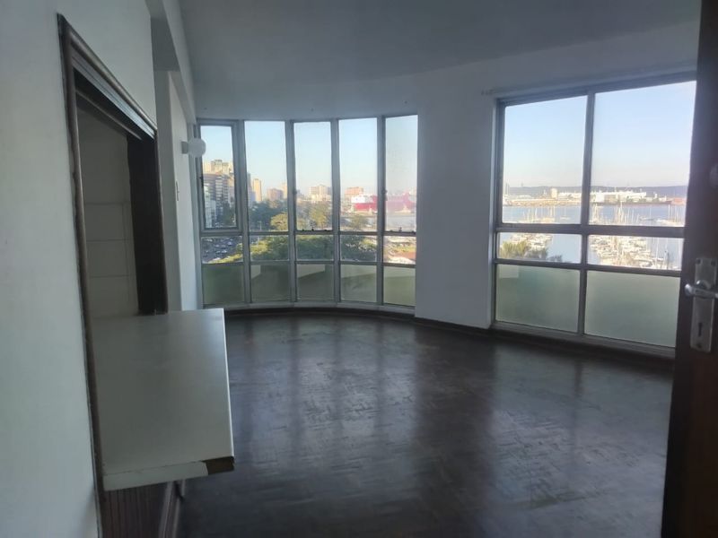 Spacious living area featuring large windows with expansive harbor views, parquet flooring, and a convenient pass-through window to the kitchen area.