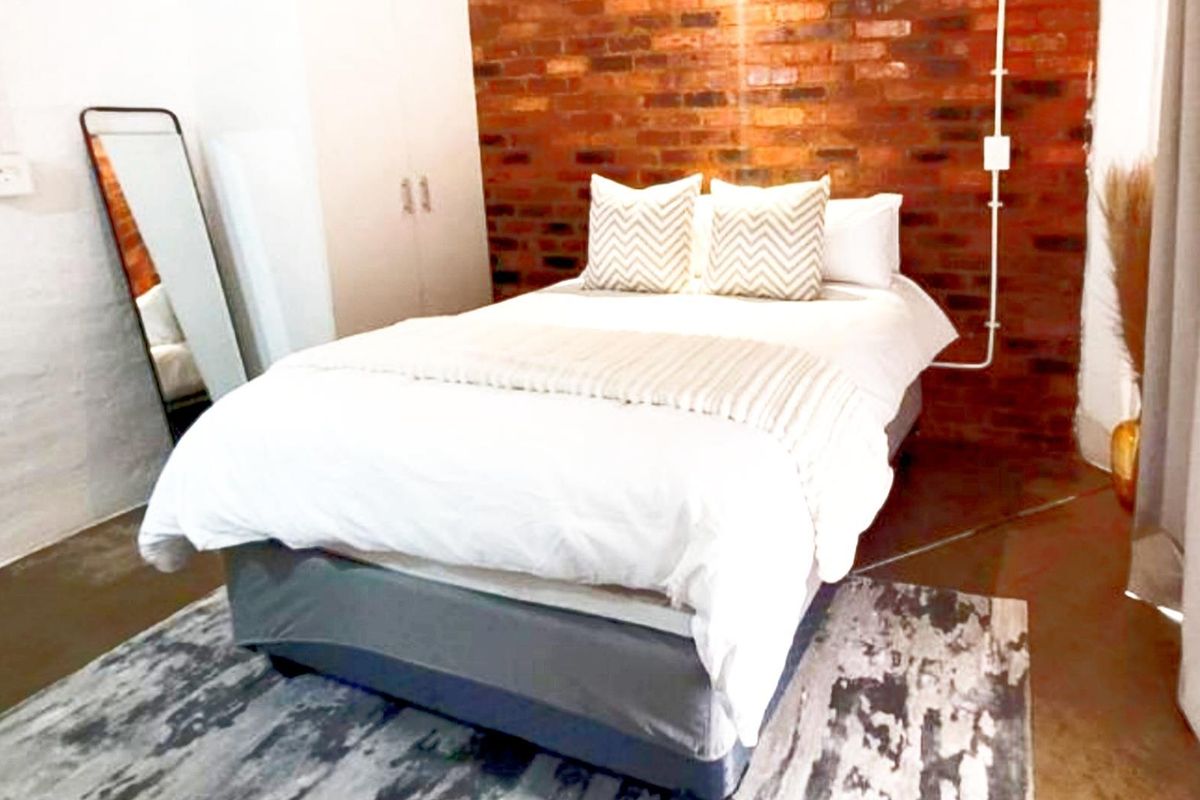 Bedroom featuring an industrial aesthetic with a prominent exposed red brick feature wall and polished concrete flooring.