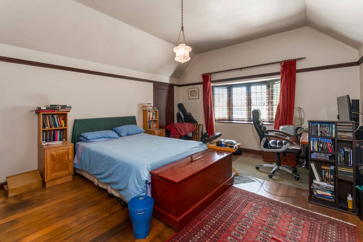 A spacious bedroom featuring polished timber flooring, a bay window, and a vaulted ceiling with a classic pendant light fixture.