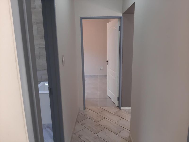 A clean, neutral hallway featuring tiled flooring and access to adjacent rooms, including a glimpse of a bathroom and bedroom.