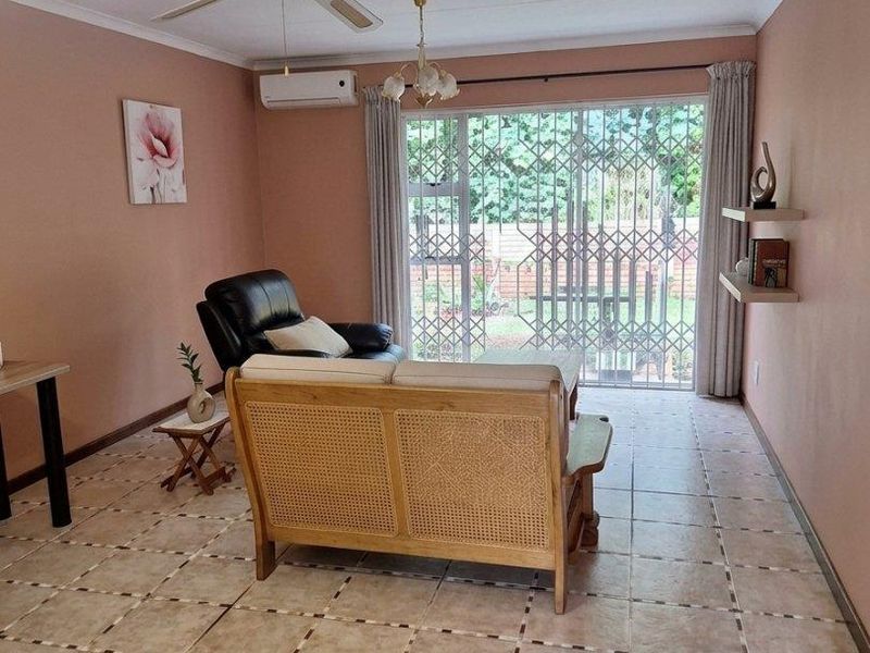 A living room featuring tiled flooring, a ceiling fan, a wall-mounted air conditioner, and a sliding glass door with a security gate leading outside.
