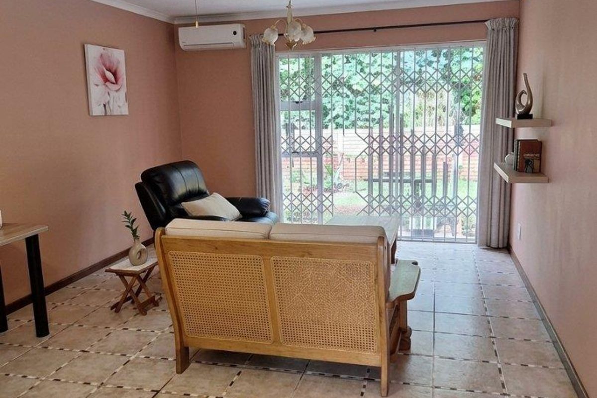 A living room featuring tiled flooring, a ceiling fan, a wall-mounted air conditioner, and a sliding glass door with a security gate leading outside.