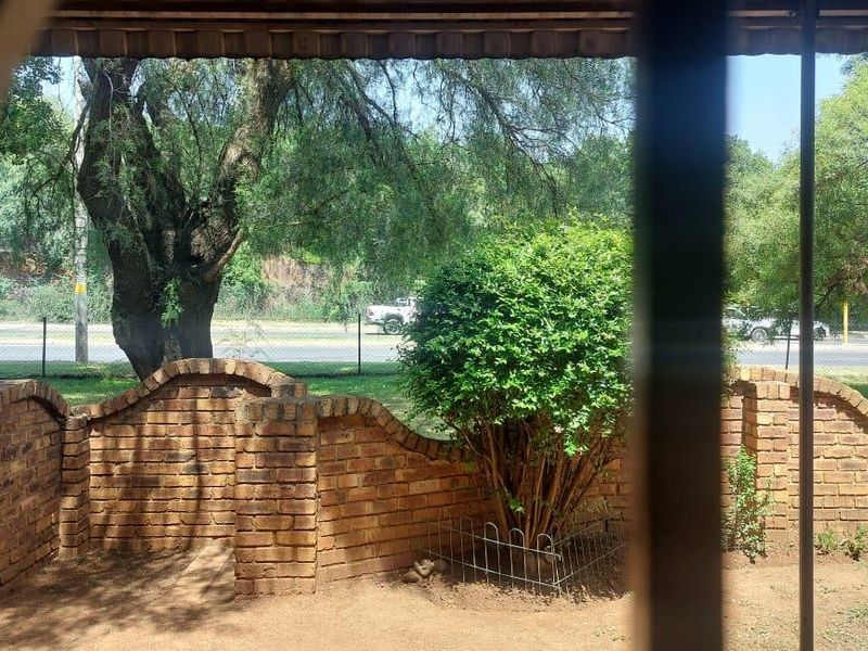 A view of a private garden area featuring a decorative brick boundary wall, viewed through security bars from inside the property.