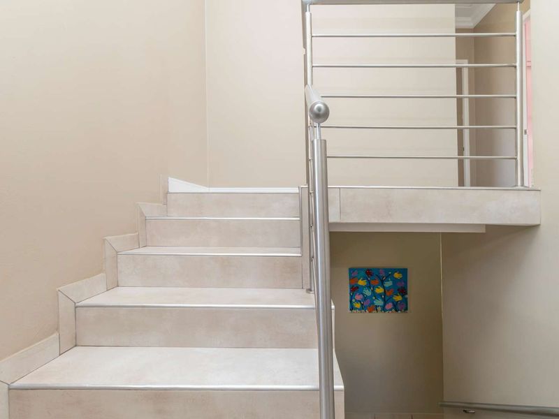 A clean, modern staircase featuring neutral-toned floor tiles and a sleek stainless steel balustrade, providing a bright and open transition between levels.