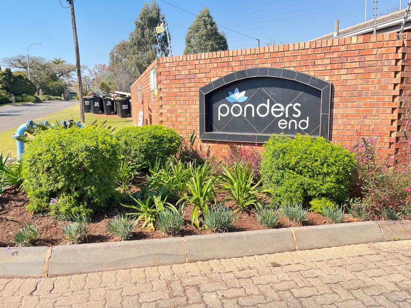 Entrance view of Ponders End complex featuring a brick boundary wall, electric fencing, and established garden landscaping.