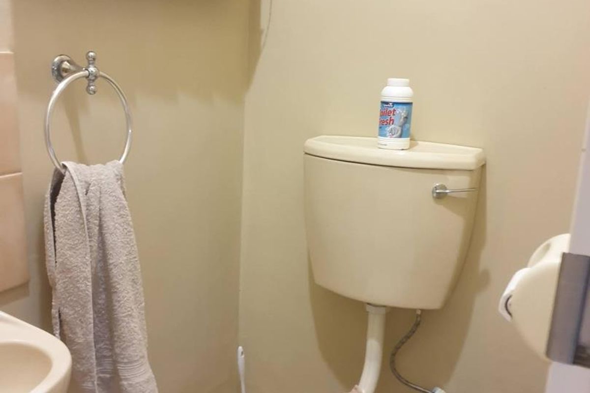 A compact bathroom featuring a standard toilet, wall-mounted basin, and neutral tile flooring.