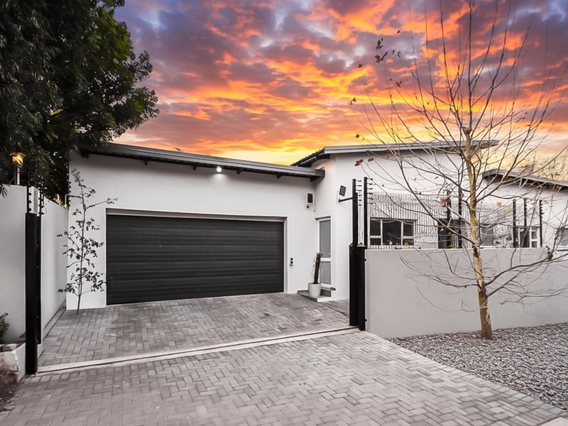 Front exterior view of the property featuring a paved driveway, automated garage, and secure boundary wall with electric fencing.