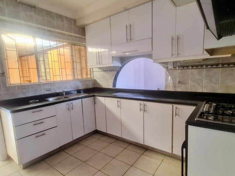 A functional kitchen featuring white cabinetry, dark countertops, a gas hob, and tiled finishes, offering a clean canvas for modern updates.
