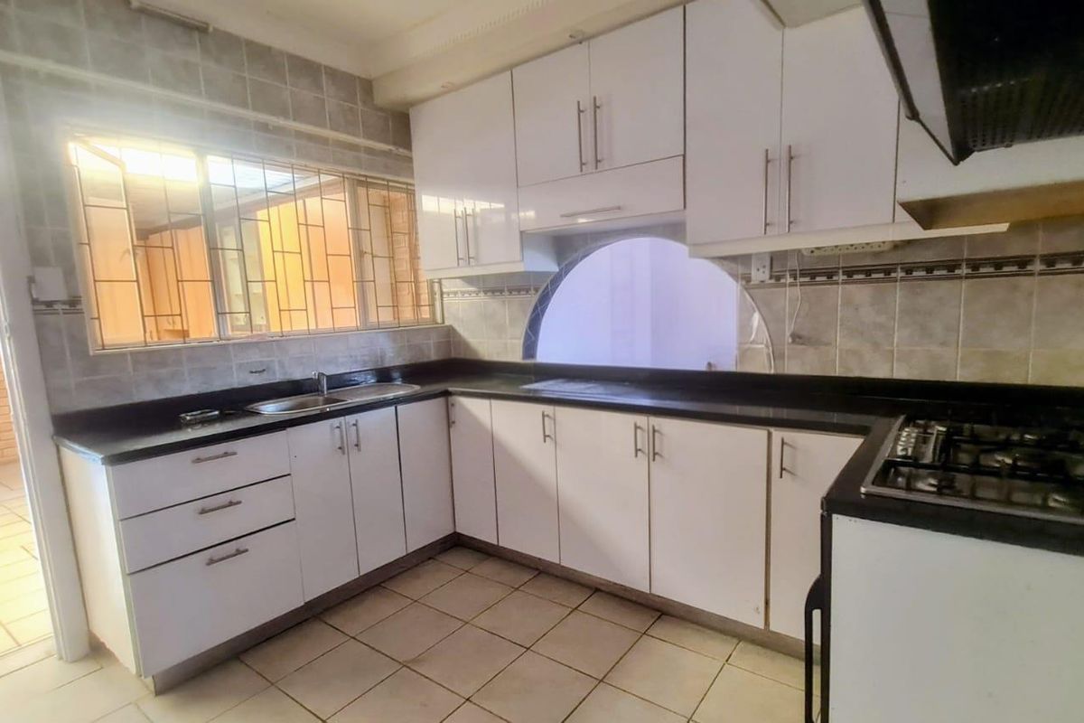A functional kitchen featuring white cabinetry, dark countertops, a gas hob, and tiled finishes, offering a clean canvas for modern updates.