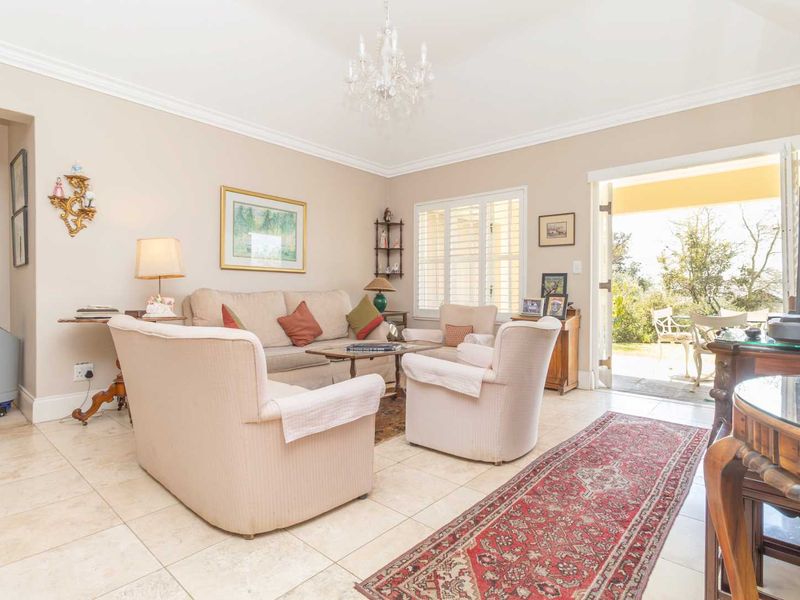 A bright living room featuring tiled flooring, crown molding, and plantation shutters, with direct access to an outdoor patio area.