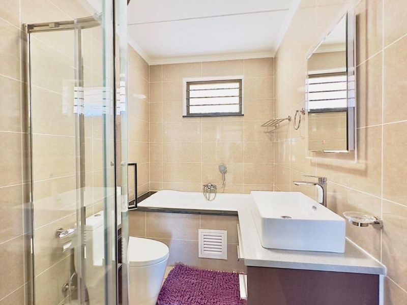 Modern bathroom featuring a glass shower enclosure, built-in bathtub, vessel sink with vanity, and neutral floor-to-ceiling tiling.