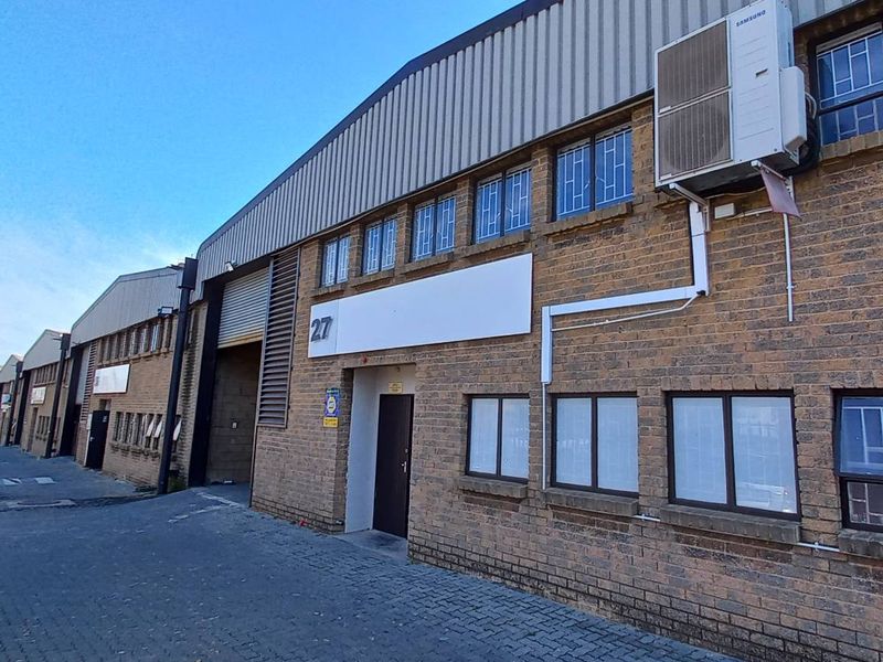 Exterior view of an industrial warehouse unit featuring face-brick facade, roller shutter door, and mounted air conditioning unit.