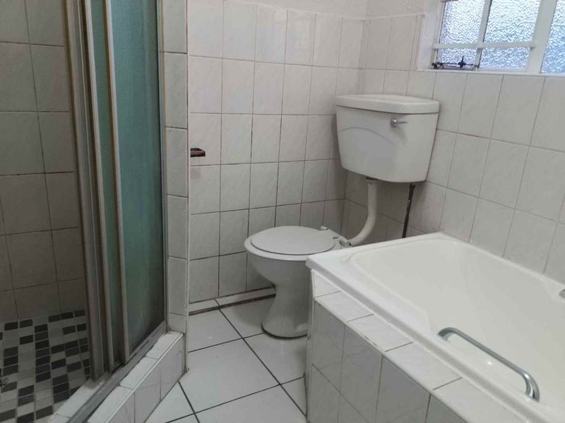 A dated bathroom featuring a shower enclosure, bathtub, and toilet with white tiled finishes and an obscured glass window.