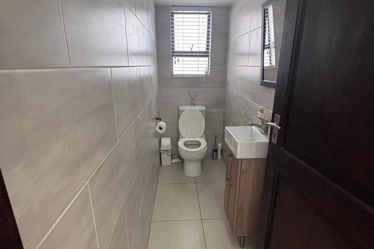 A modern, narrow guest bathroom featuring floor-to-ceiling neutral wall tiles, a vanity basin, and a toilet.