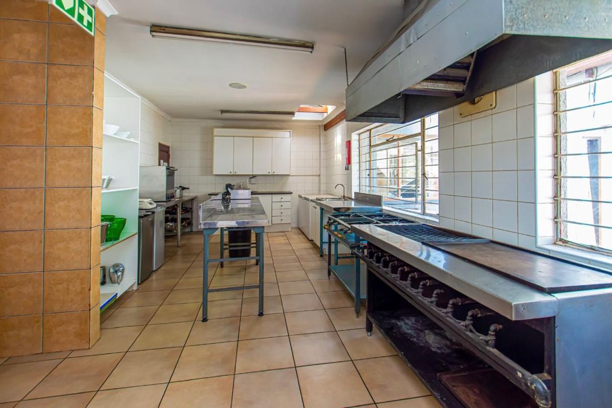 A functional commercial-style kitchen featuring stainless steel work surfaces, a large gas range with extractor hood, and tiled flooring.
