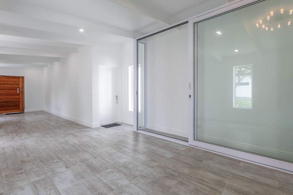 A bright, spacious, and empty living area featuring modern tiled flooring, recessed lighting, and large sliding glass doors leading to an outdoor space.