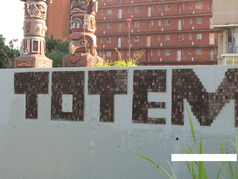 Exterior view of a concrete boundary wall featuring decorative totem poles and building signage in front of a multi-story apartment complex.