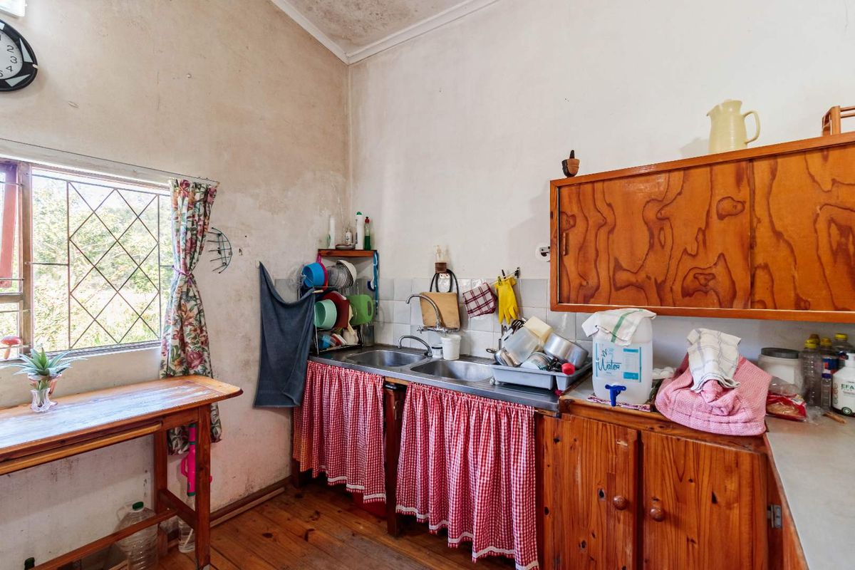 A dated kitchen area featuring wooden cabinetry, a double stainless steel sink, and timber flooring, requiring significant cosmetic updates and maintenance.
