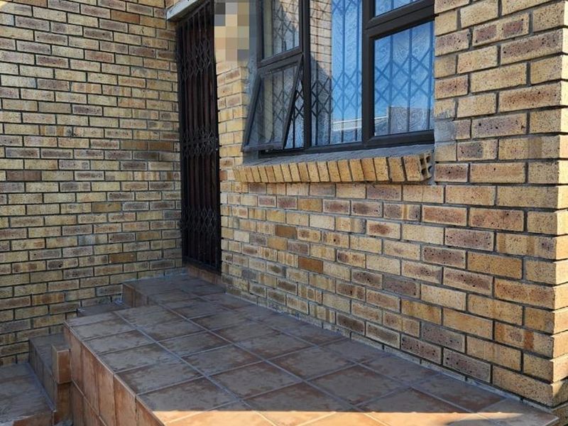 A rear exterior view featuring a face brick facade, a tiled patio area, and secure window and door fittings.