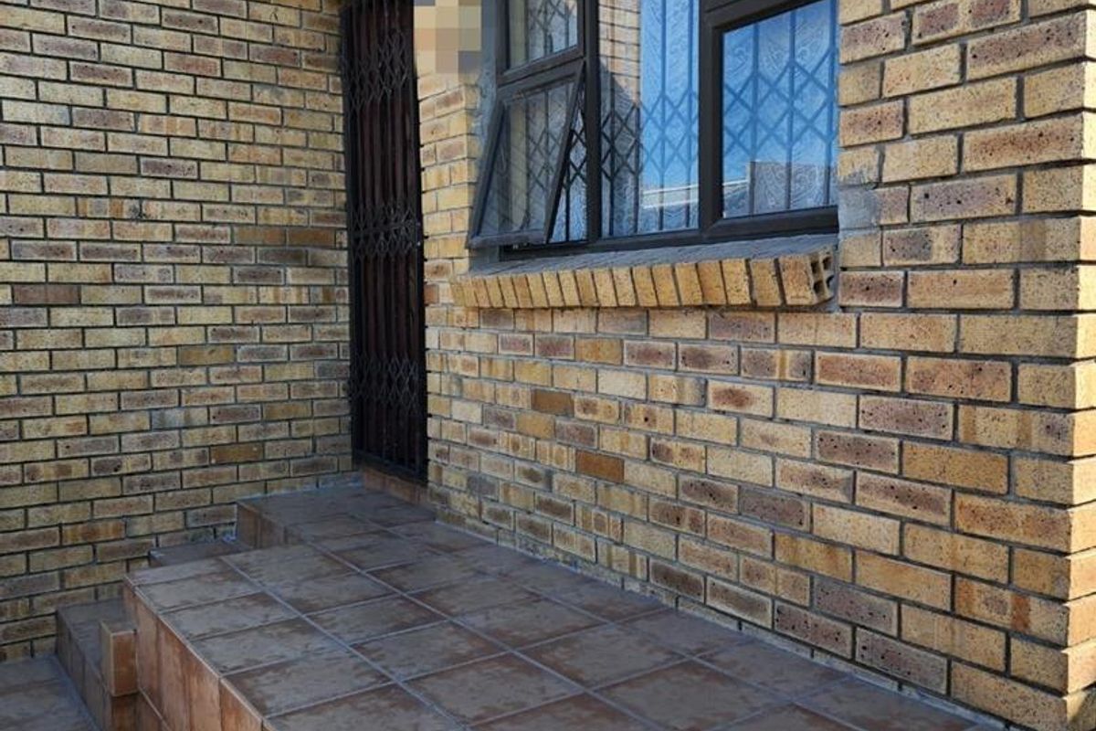 A rear exterior view featuring a face brick facade, a tiled patio area, and secure window and door fittings.