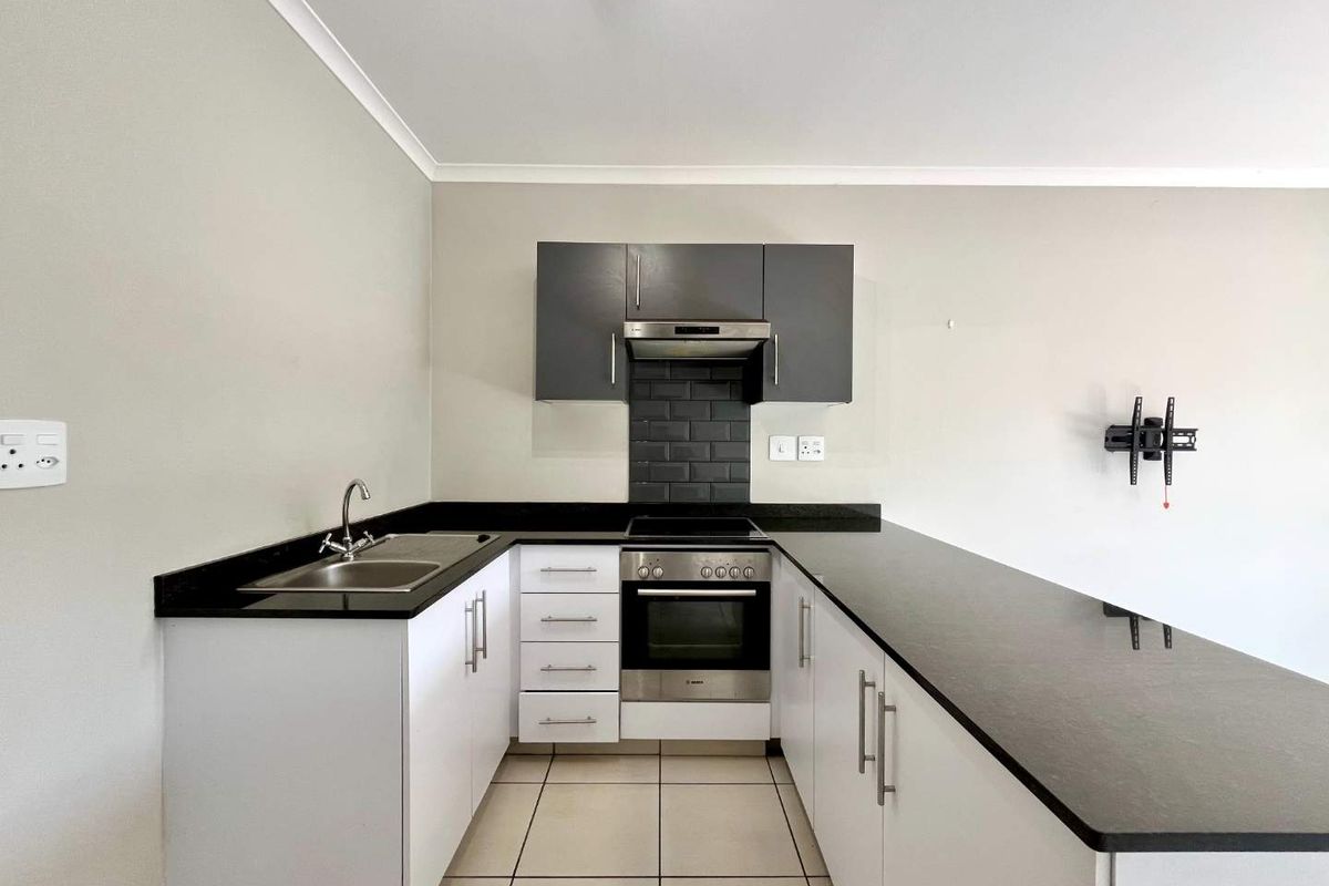 A modern, clean kitchen featuring white cabinetry, black granite countertops, a built-in oven, hob, and extractor fan with a tiled backsplash.