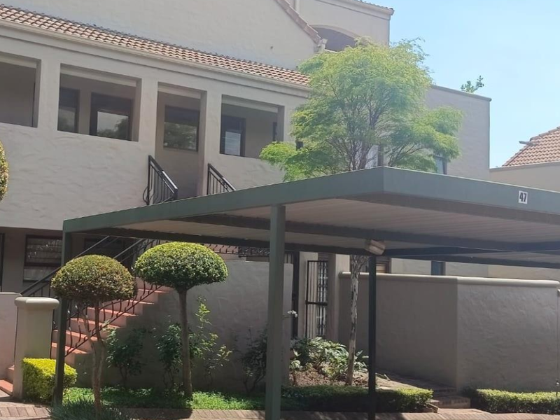 Exterior view of an apartment complex featuring a covered carport, paved driveway, and external staircase leading to upper-level units.