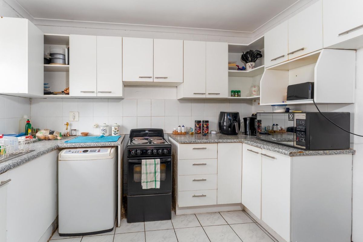 Functional kitchen featuring white cabinetry, granite-look laminate countertops, tiled backsplash, and space for a freestanding stove and washing machine.