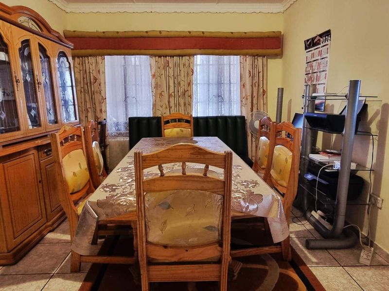 A dining room featuring tiled flooring, decorative cornicing, and a serving hatch connecting to the adjacent kitchen area.