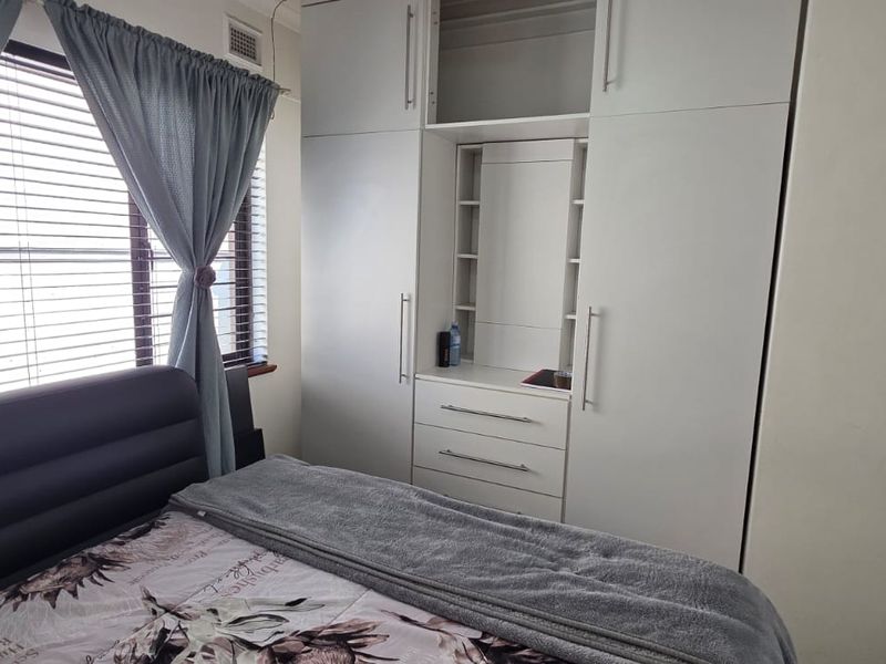 A bedroom featuring a large white built-in wardrobe with an integrated vanity unit and venetian blinds.