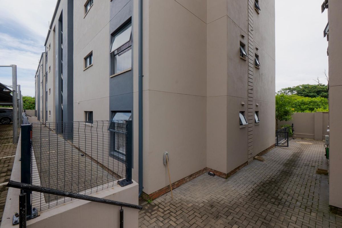 Exterior view of the apartment building showing paved walkways, perimeter fencing, and modern facade finishes.