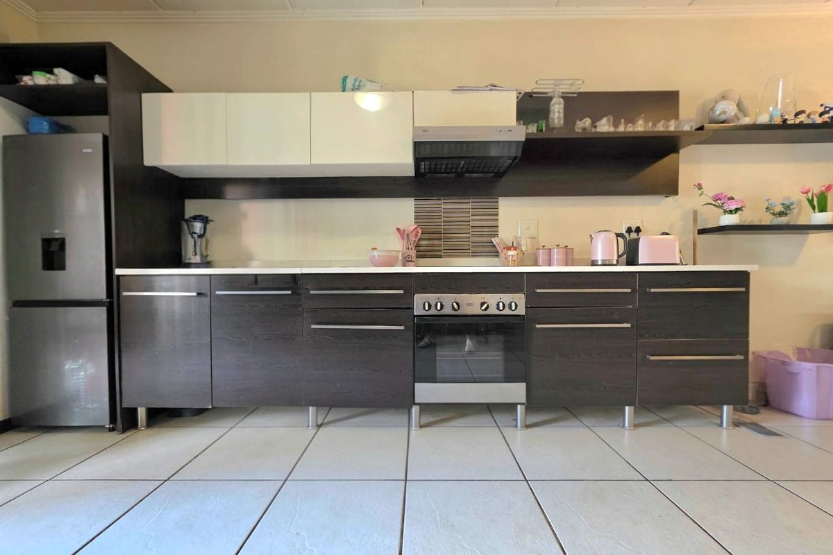 A modern kitchen featuring dark wood-grain cabinetry, white upper cabinets, a built-in oven with extractor fan, and light-colored tiled flooring.