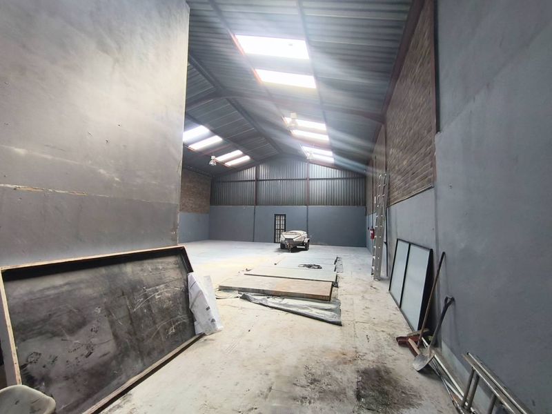 Spacious industrial utility area featuring high ceilings with skylights, exposed steel trusses, and durable concrete flooring, suitable for various commercial or storage applications.