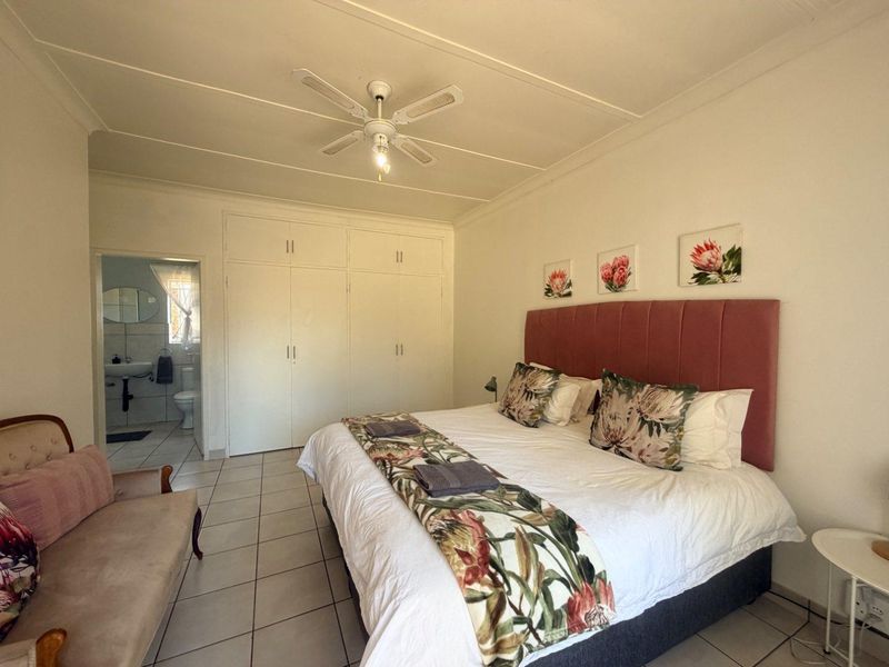 Spacious bedroom featuring built-in cupboards, tiled flooring, a ceiling fan, and direct access to an en-suite bathroom.